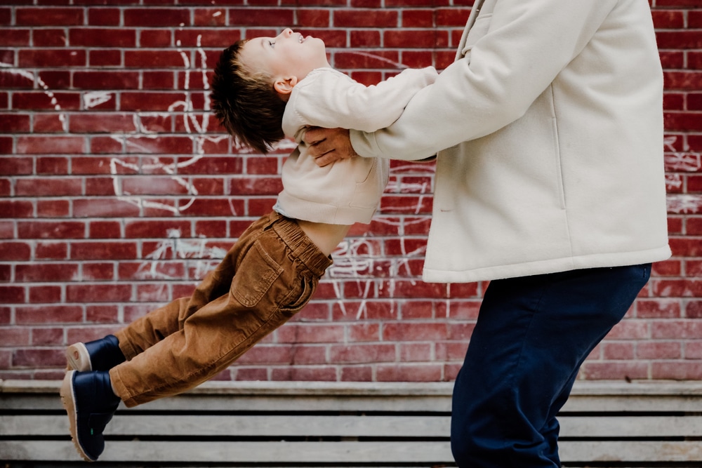 photographe famille paris papa qui fait voler son petit garcon devant un mur en brique